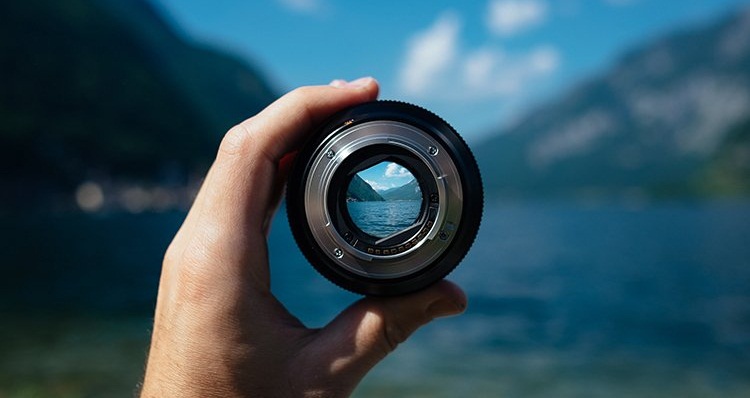 Photo d'un objectif focale fixe tenu dans une main et où la mise au point est faite sur le paysage vu dans l'objectif