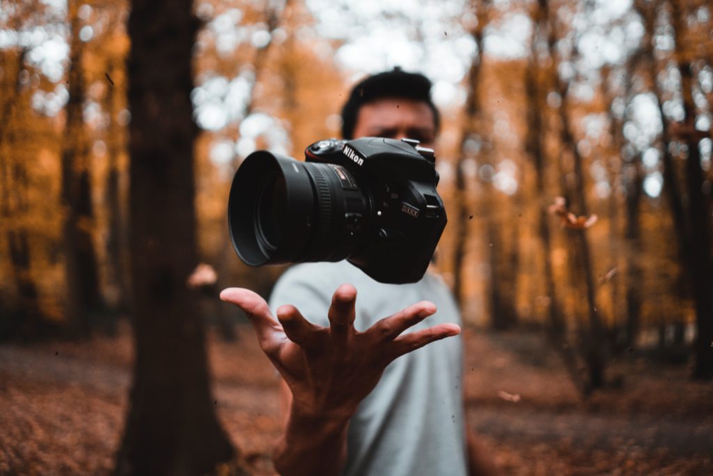 Photo d'un appareil photo en l'air, jeté par un jeune homme dans un bois en automne