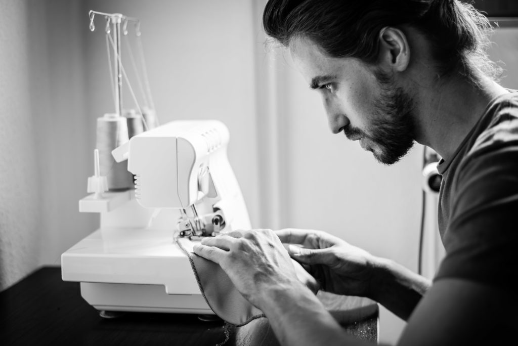 Photo en noir et blanc représentant un portrait de profil d'un homme travaillant sur une machine à coudre