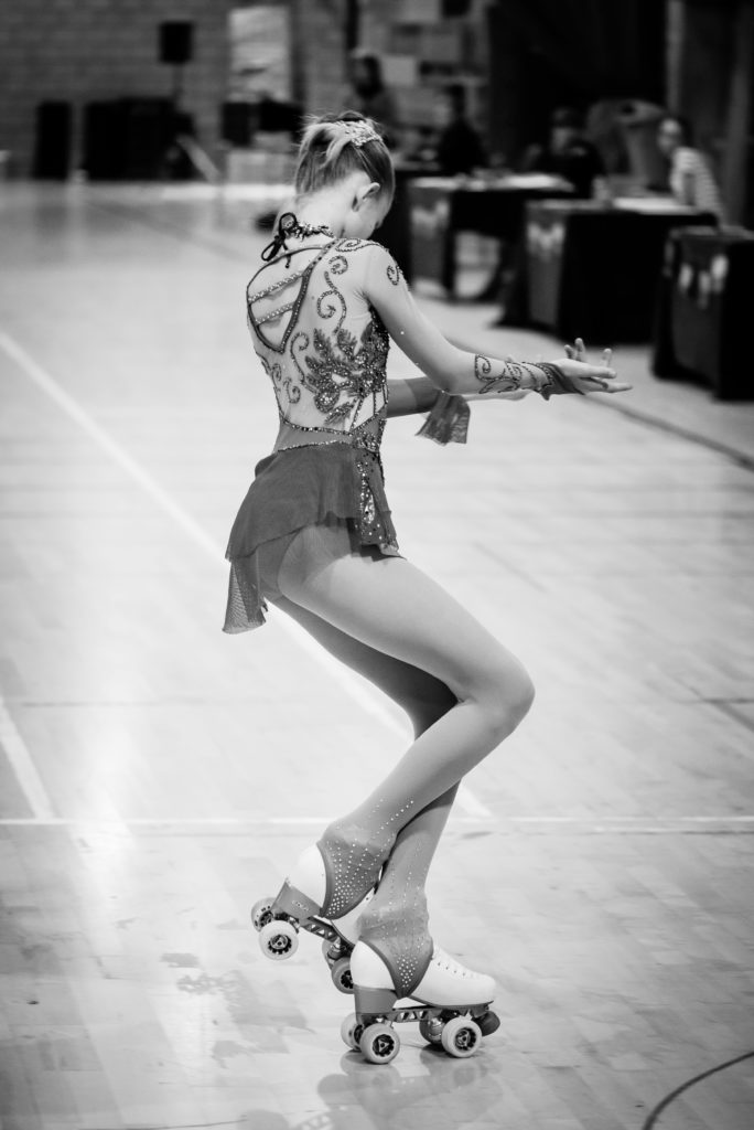 Photo en Noir et Blanc d'une patineuse en salle, prise de dos avec une pose artistique