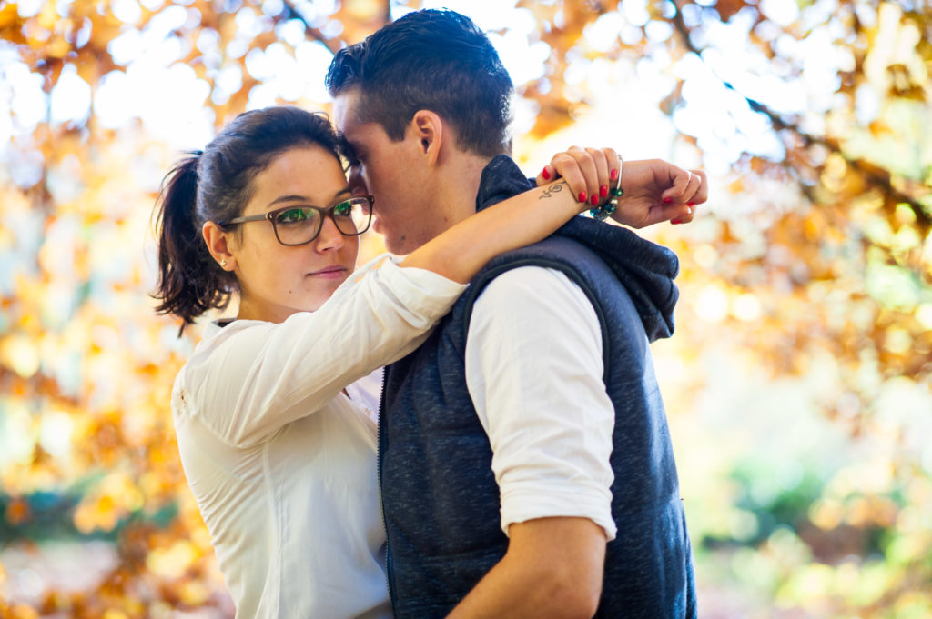 Photo couleur d'un couple qui s'enlace, pris de près avec en arrière-plan une végétation automnale