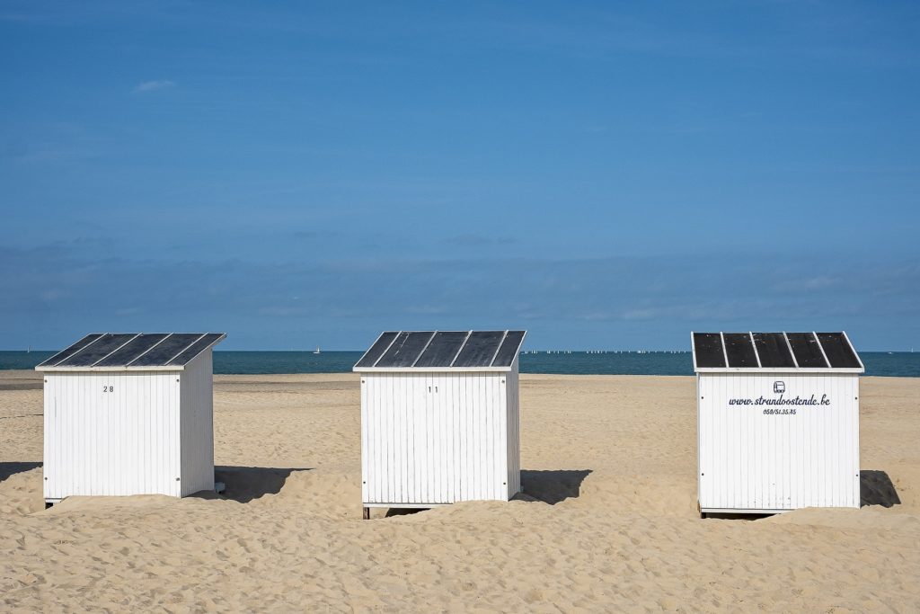 Une vue frontale d'une plage avec trois cabines et des voiliers sur l'eau à l'horizon