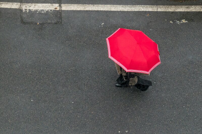 Photo couleur prise en plongée et représentant une personne qui se balade dans la rue sous un parapluie rouge